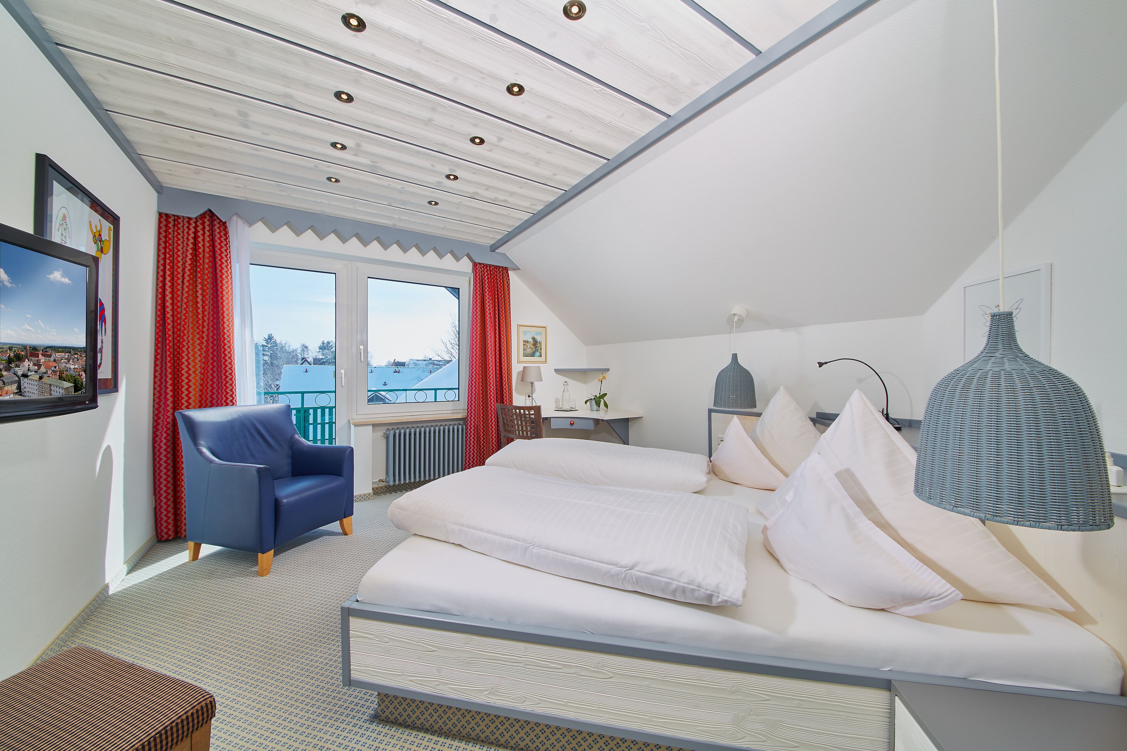 A bedroom with a large bed, a chair, a desk, and a window with curtains.