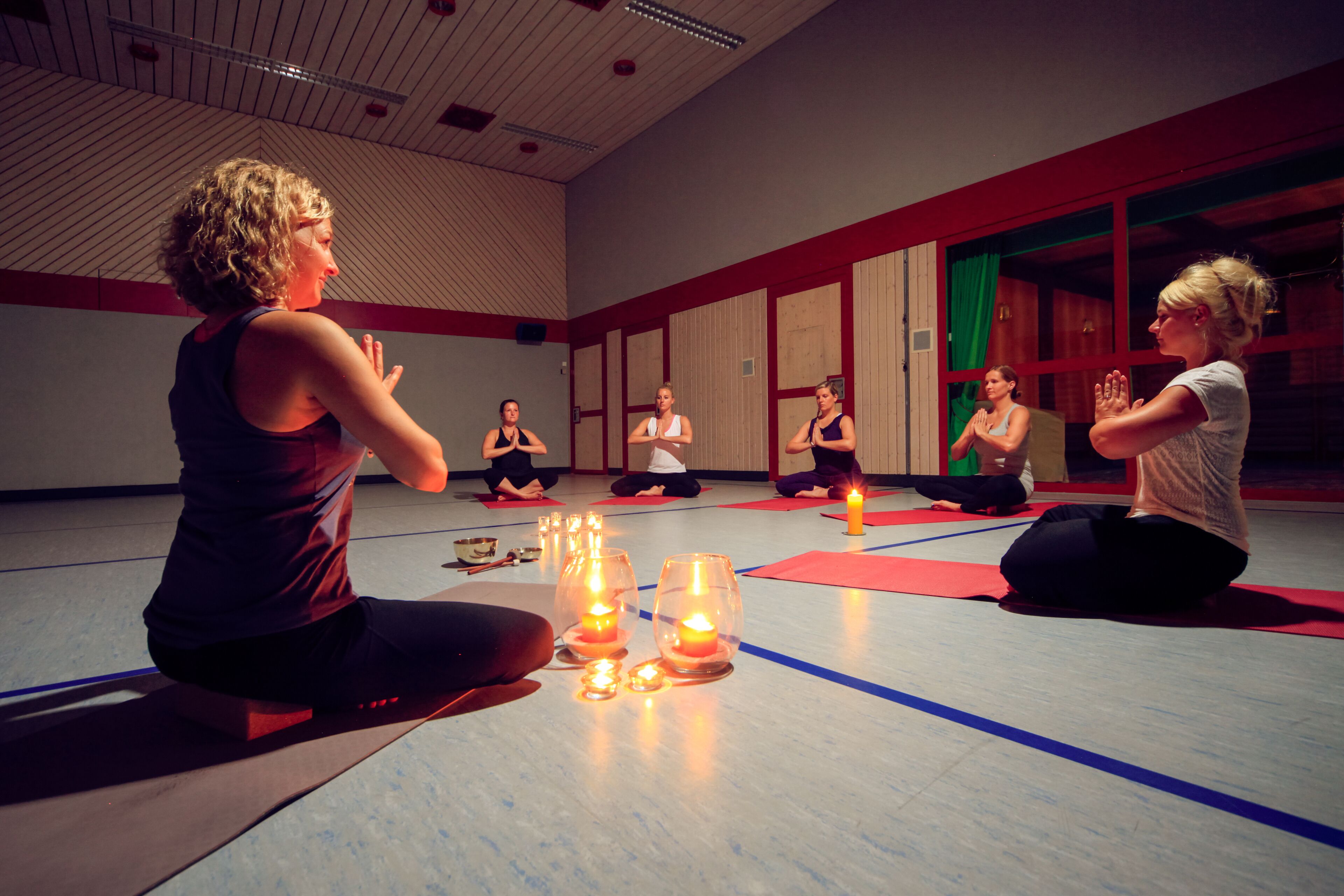 Un grupo de personas sentadas sobre esterillas de yoga en una habitación con paredes de madera y un techo alto.