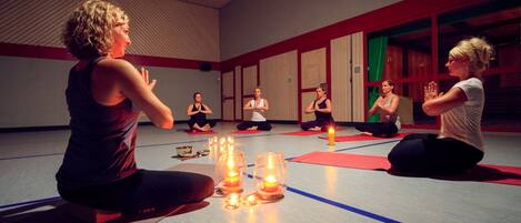 Un grupo de personas sentadas sobre esterillas de yoga en una habitación con paredes de madera y un techo alto.