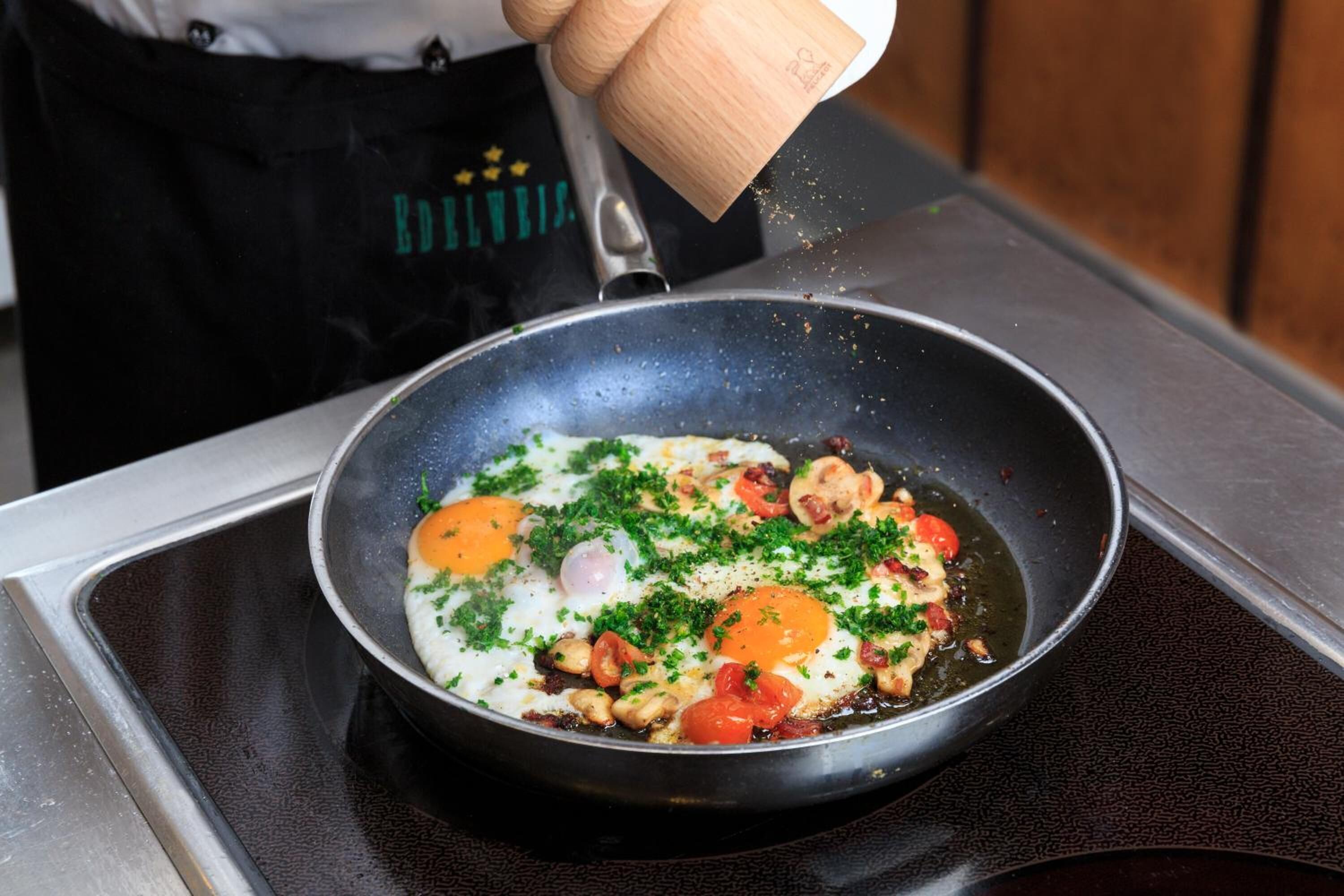 Ein Koch bereitet Eier mit Tomaten und Kräutern in einer Pfanne zu.