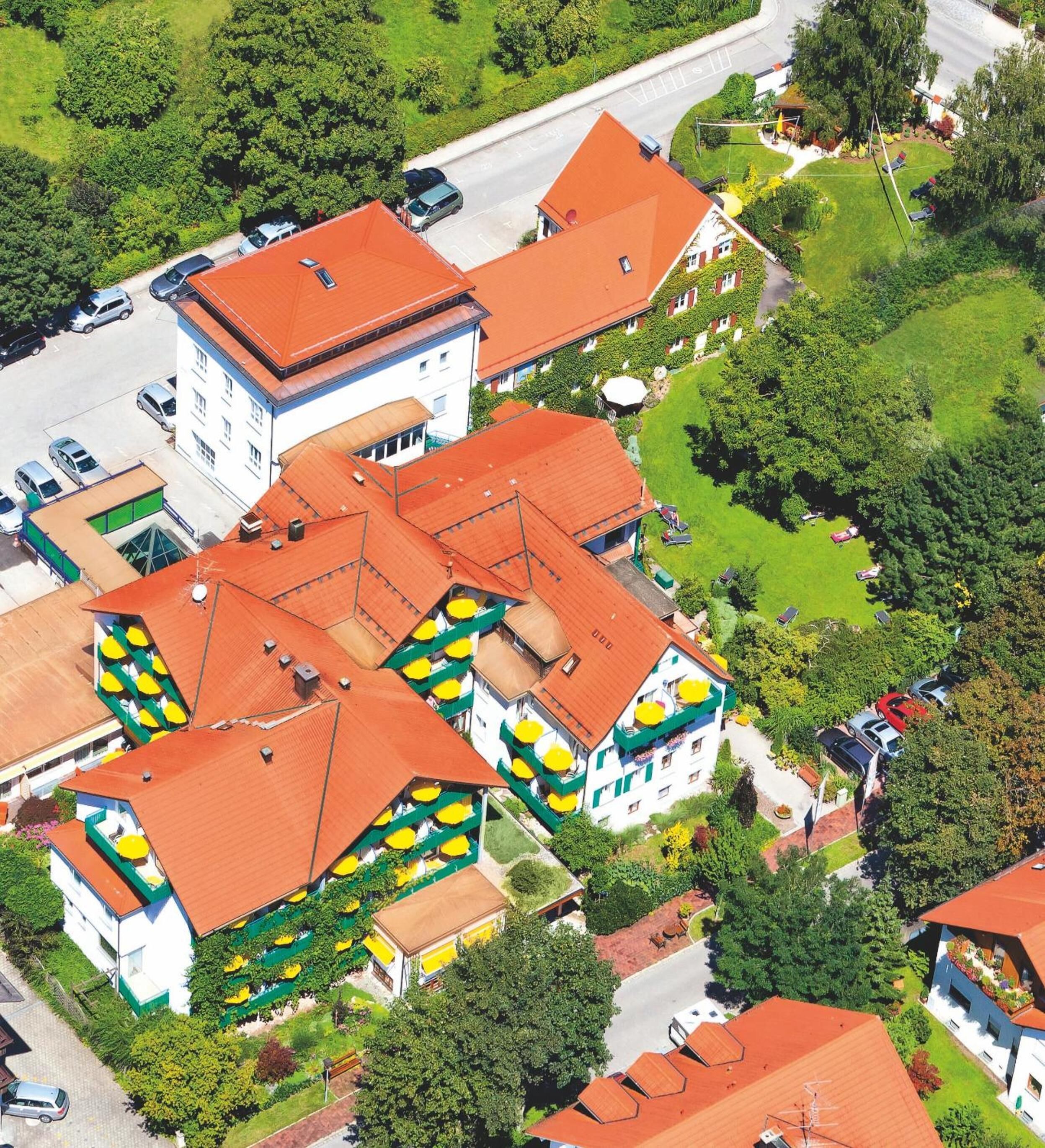 A multi-story building with a red roof, surrounded by greenery and a road.