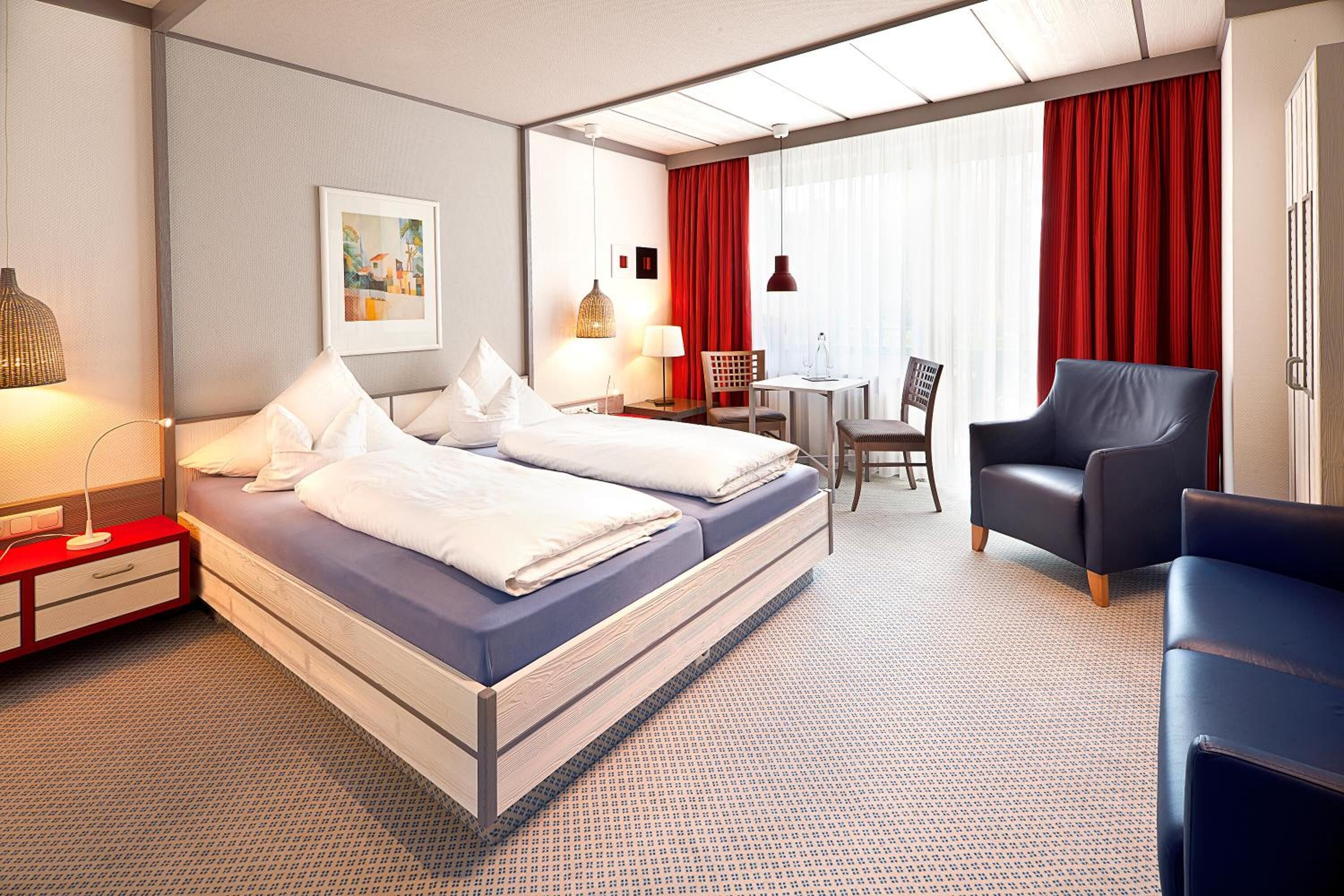 A hotel room with a large bed, a desk, a chair, and a sofa.