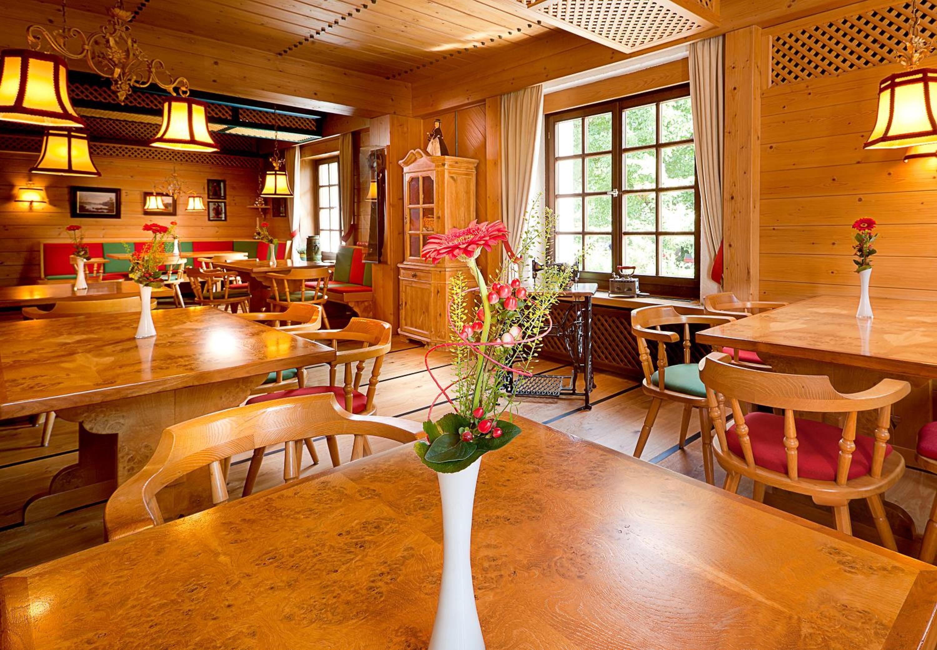 A wooden interior with tables and chairs, a vase with flowers, and a window with curtains.