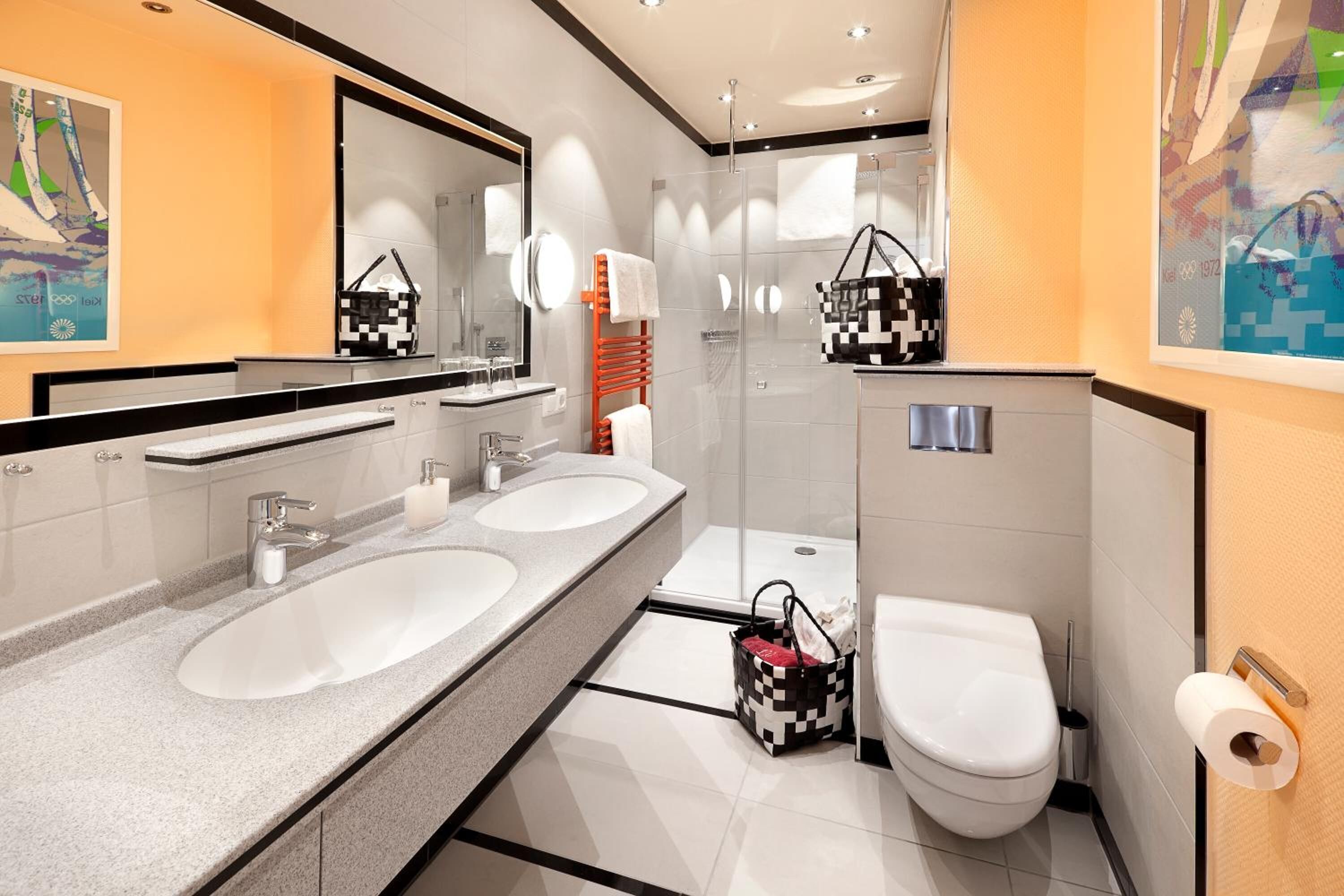Ein modernes Badezimmer mit zwei Waschbecken, einem großen Spiegel, einer Duschkabine aus Glas und einer Toilette.