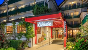 A hotel entrance with a red awning, a stone statue, and a staircase leading to the entrance. - Kneipp- und Wellvitalhotel Edelweiss (Bad Woerishofen)
