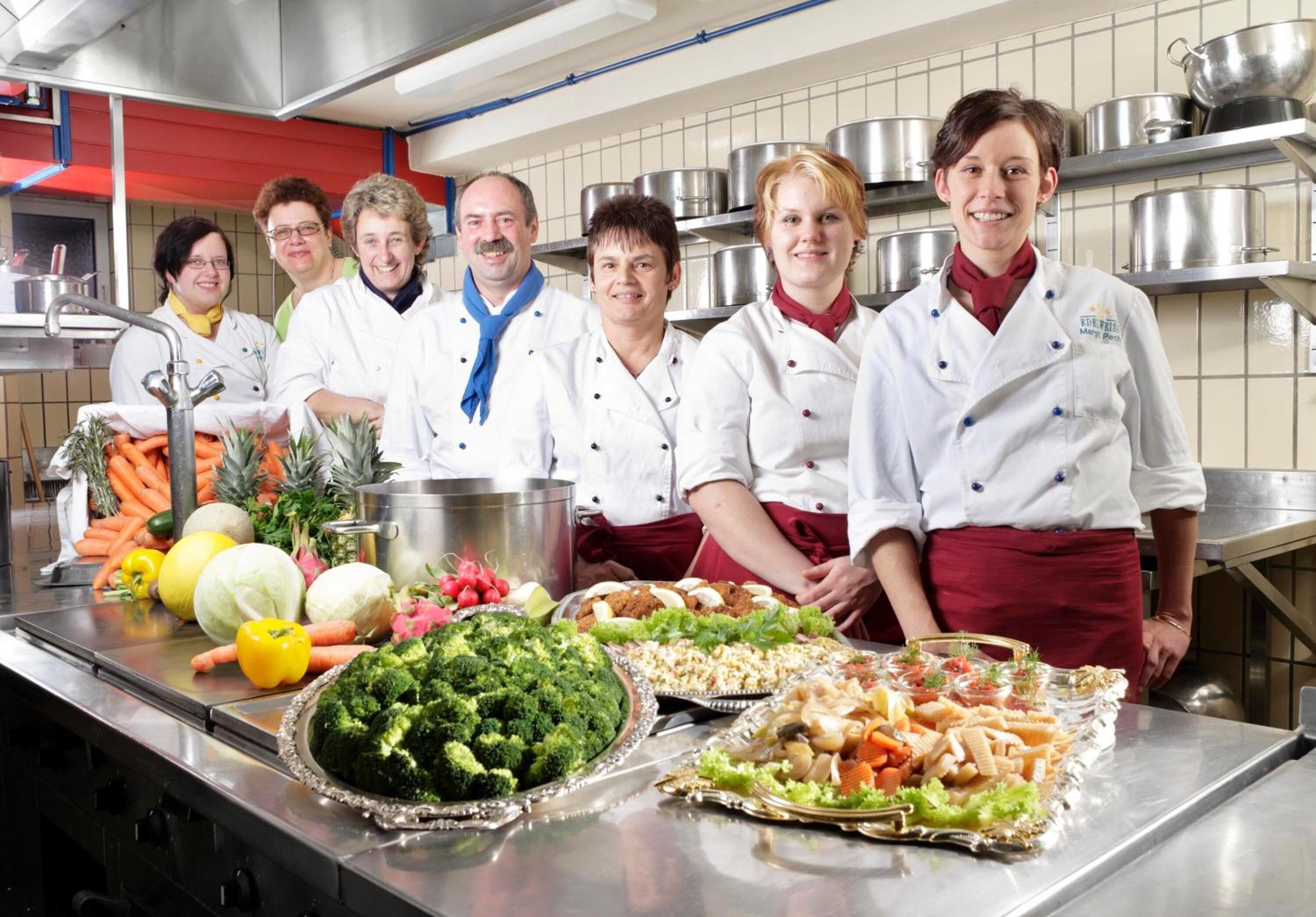 Un grupo de cocineros en una cocina con diversos vegetales y utensilios de cocina.