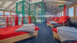 A spa area with wicker beds, red cushions, and a glass enclosure with plants. - Kneipp- und Wellvitalhotel Edelweiss (Bad Woerishofen)