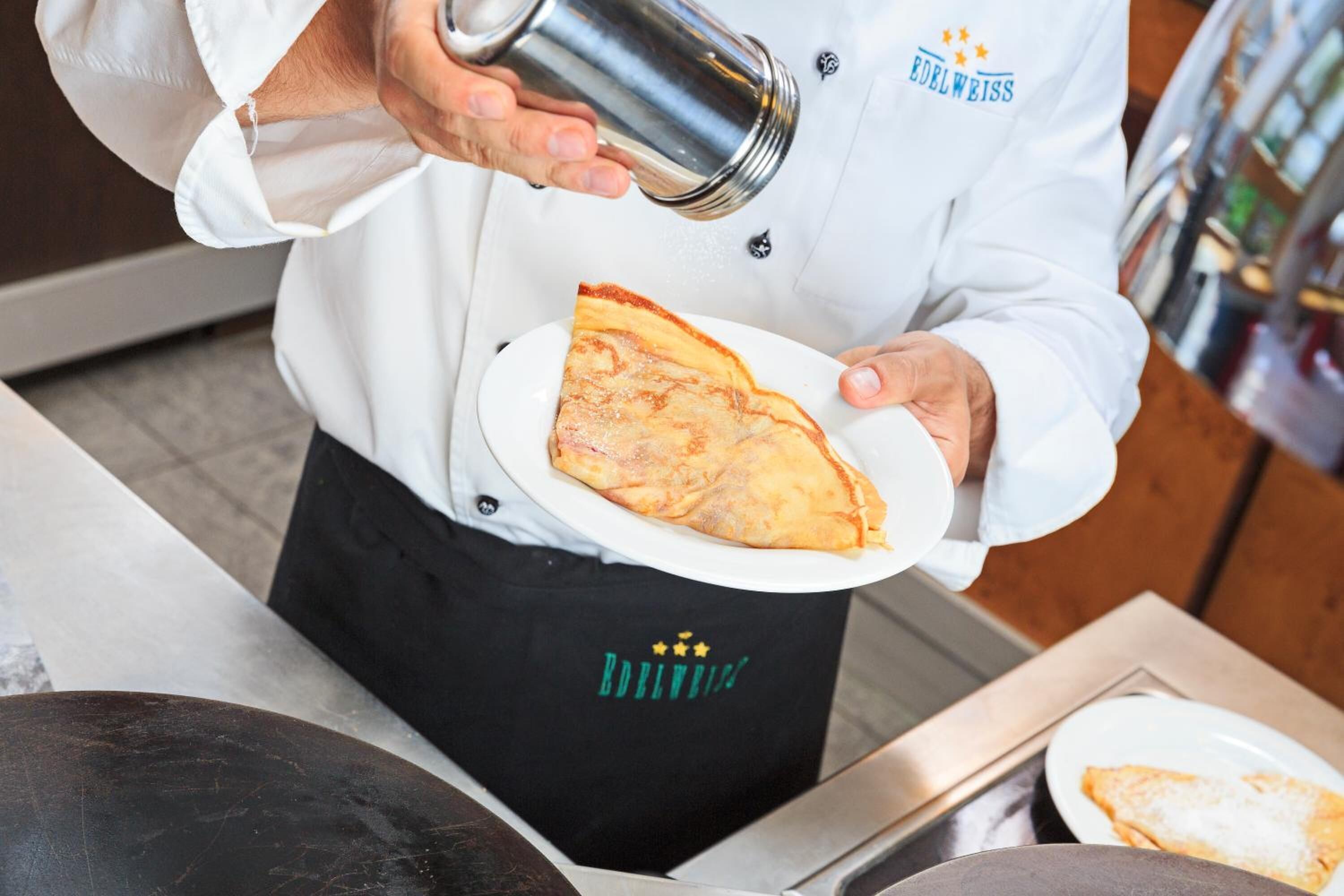 Una persona con uniforme blanco y el logo 'Edelweiss' sirviendo una bebida en un plato blanco con una porción de pizza.
