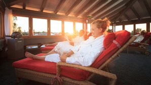 A room with wicker lounge chairs, red cushions, and large windows with a view. - Kneipp- und Wellvitalhotel Edelweiss (Bad Woerishofen)