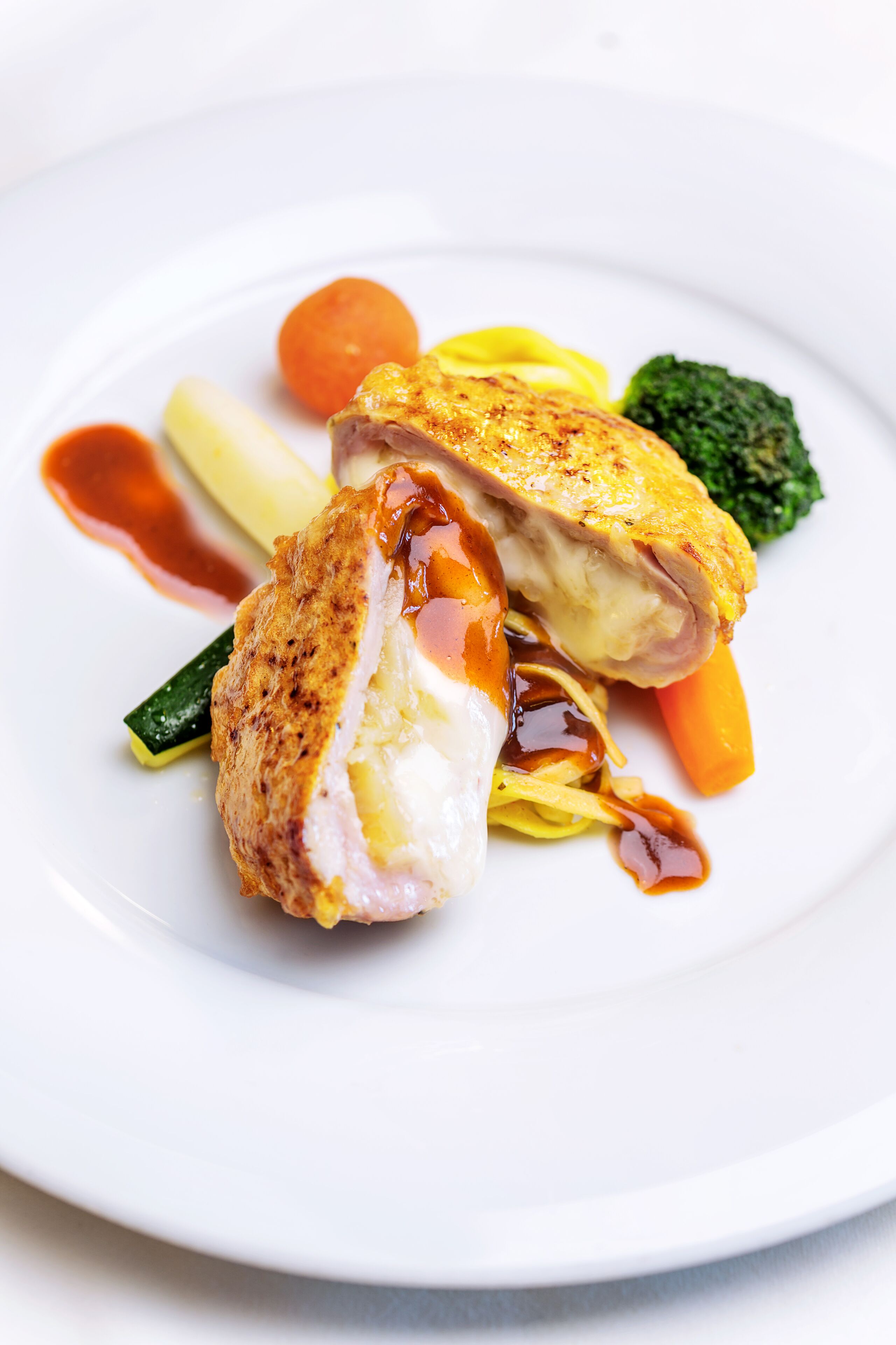 A white plate with a piece of grilled chicken, vegetables, and sauce.