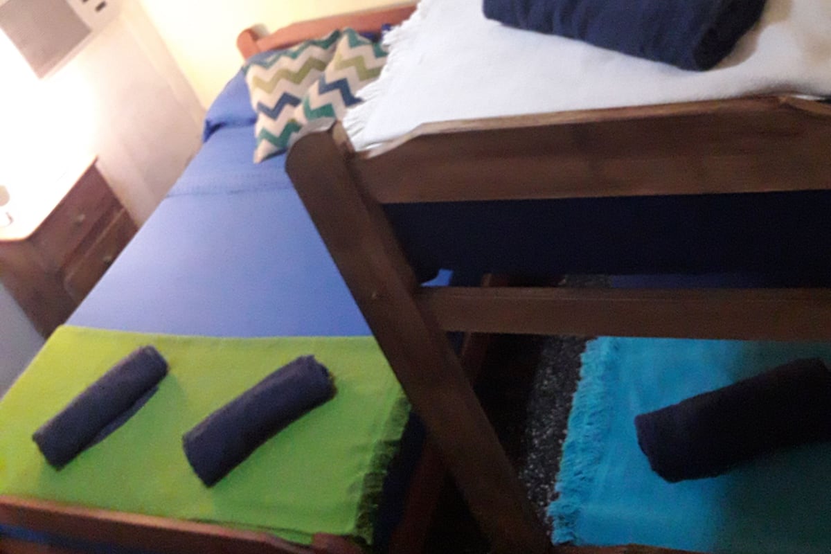Una habitación con dos camas, una con colchón azul y otra con colchón blanco. Hay almohadas y una manta en las camas.