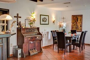 Un comedor con un piano, sillas, una mesa y obras de arte en la pared.