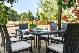 Un espacio de comedor al aire libre con sillas de mimbre y una mesa para dos, rodeado de follaje y una valla de madera.