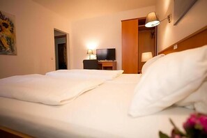 Habitación de hotel con dos camas, una televisión y un escritorio con lámpara.