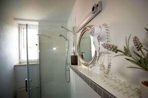 Un baño con cabina de ducha de vidrio, un secador de pelo montado en la pared y un espejo con marco decorativo.