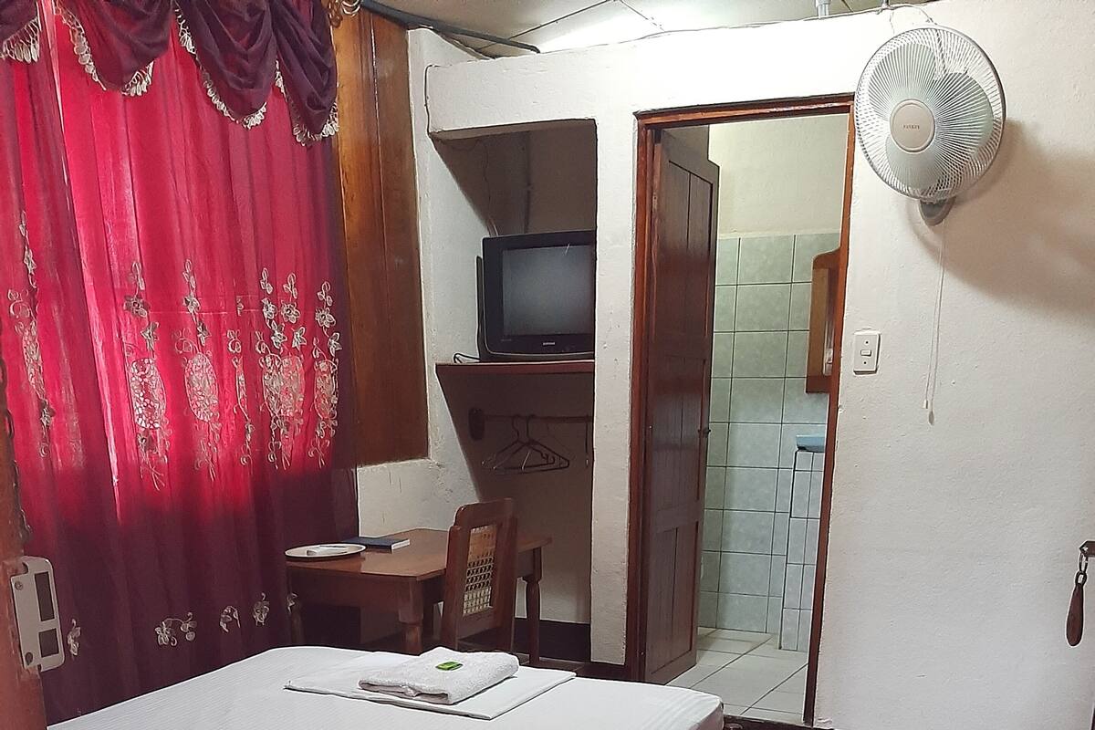 Ein Schlafzimmer mit einem Einzelbett, einem Fernseher, einem Schreibtisch und einem Spiegel.