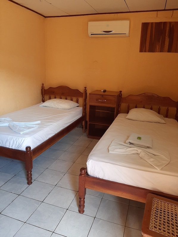 A room with two wooden beds, a nightstand, an air conditioning unit, and a tiled floor. - Hotel Cabinas Leyko (San Carlos)
