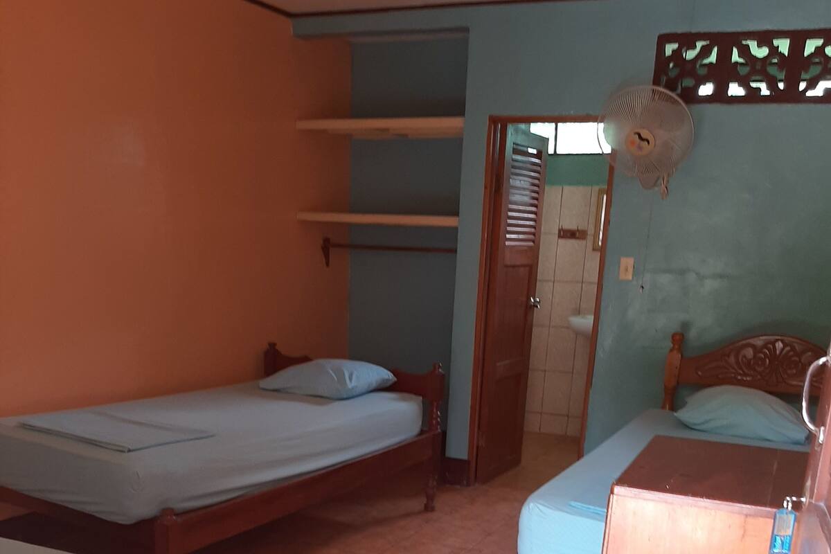 Ein Zimmer mit zwei Einzelbetten, einem Holzschrank und einem Ventilator.