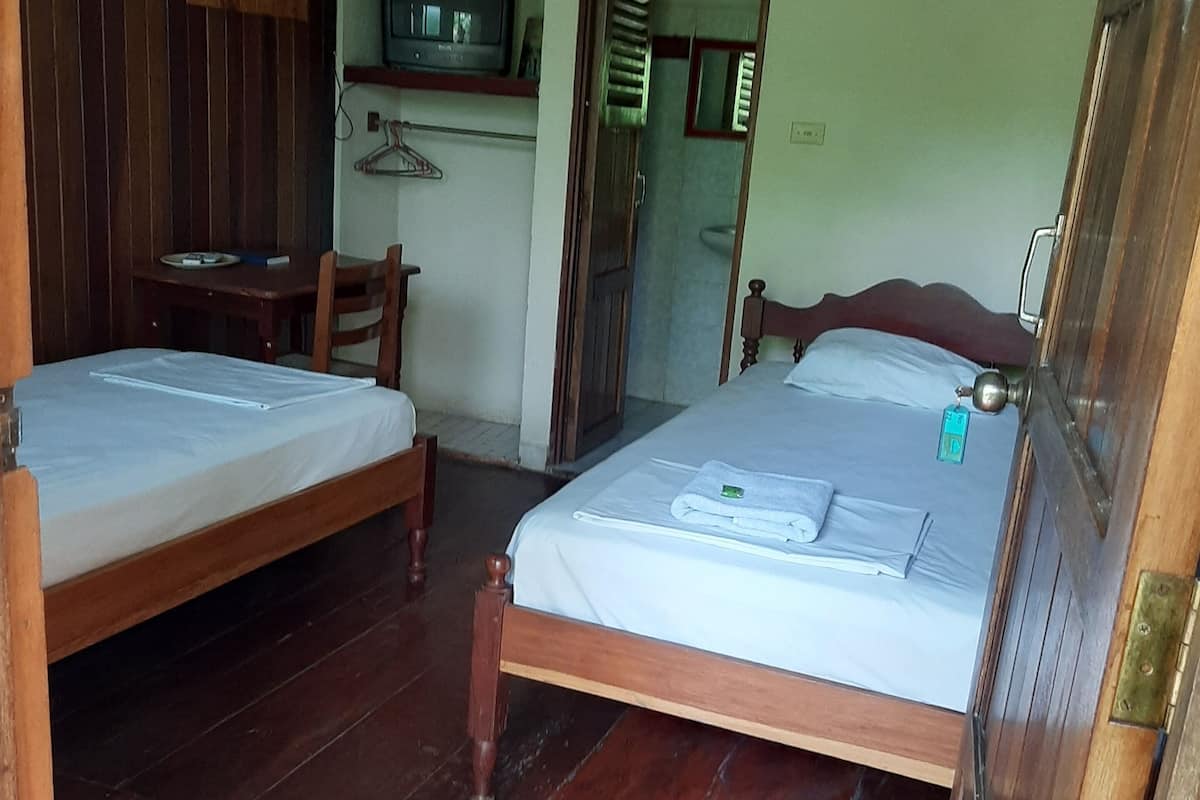 Ein Zimmer mit zwei Holzbett, einem an der Wand befestigten Fernseher und einer Holztür.