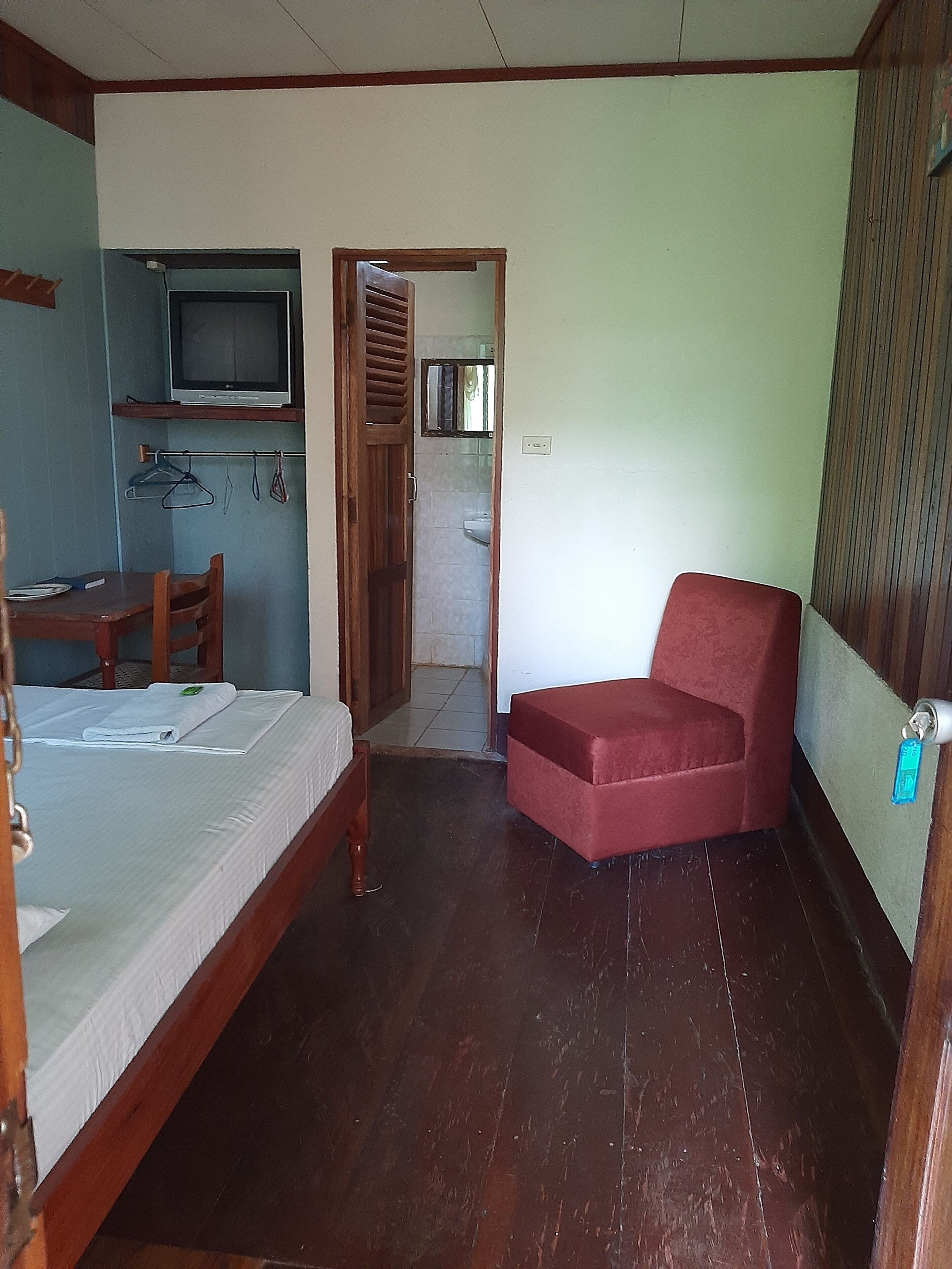 A room with a bed, a red chair, a TV, and a bathroom visible through an open door.