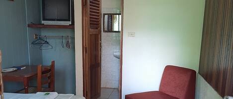 A room with a bed, a red chair, a TV, and a bathroom visible through an open door.