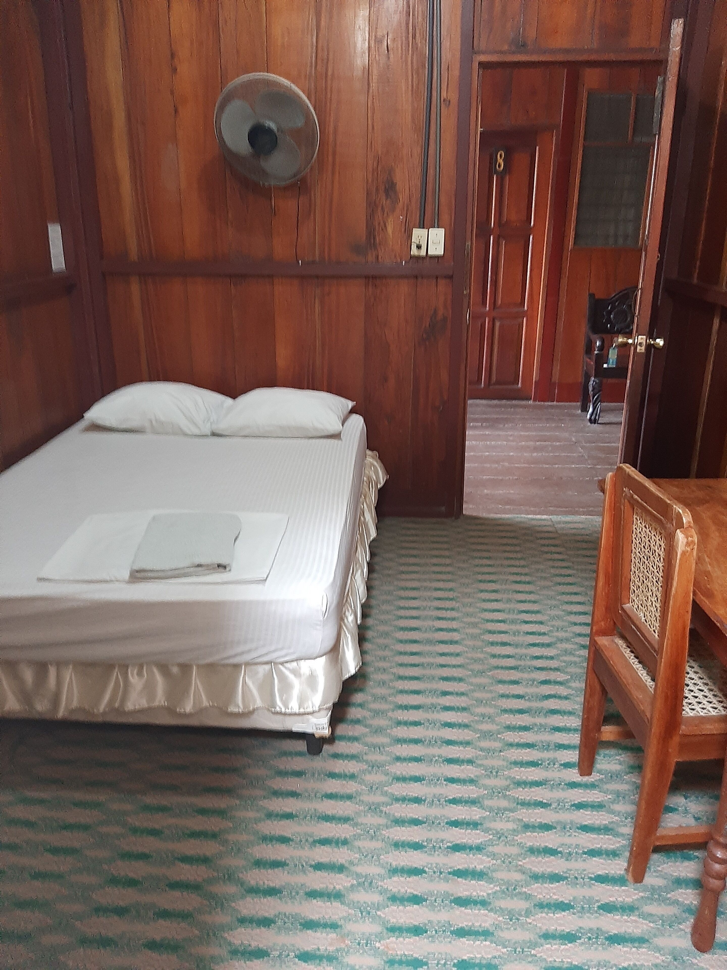 Een kamer met een houten bed, een stoel en een deur naar een andere kamer.