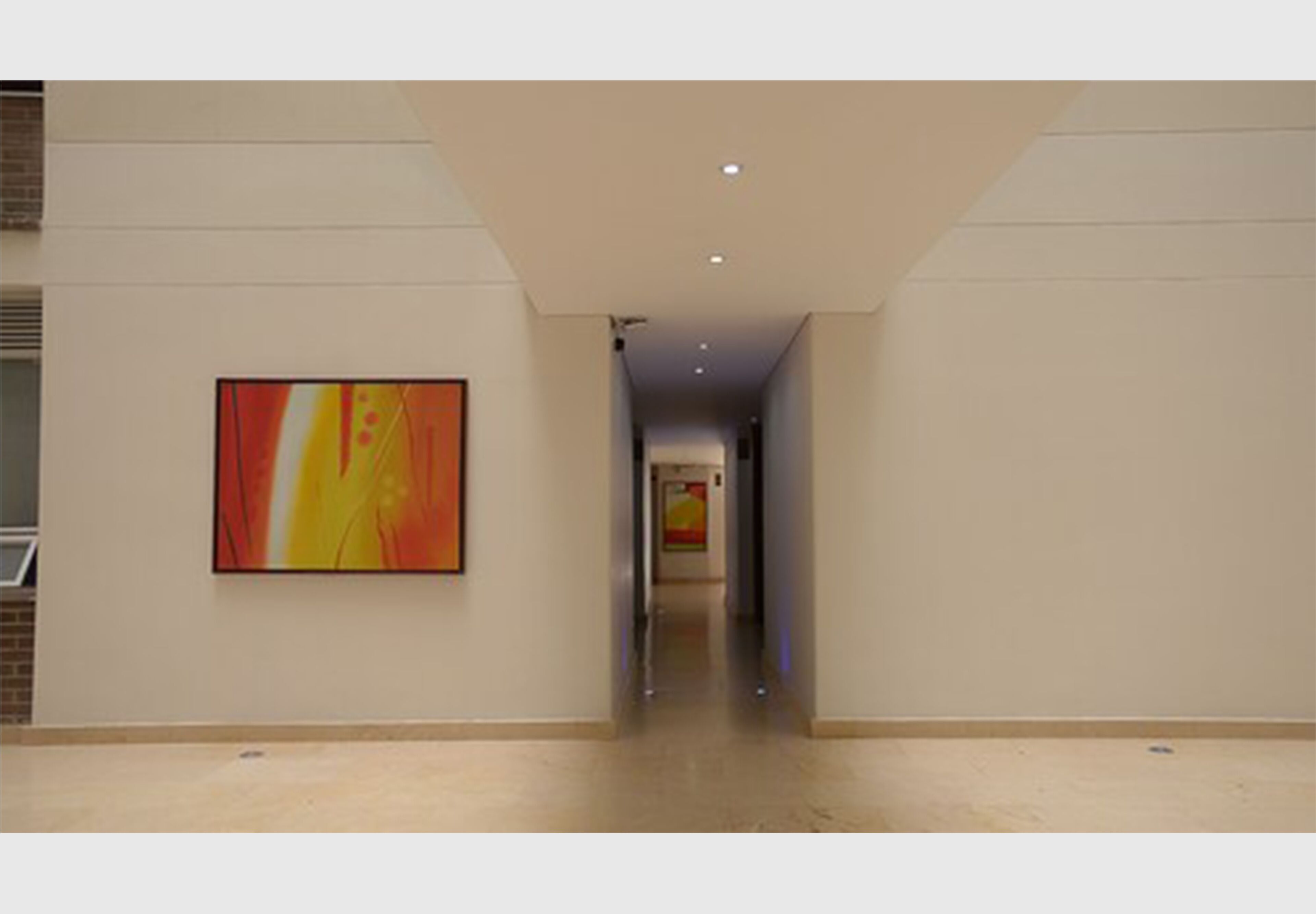 A hallway with a large abstract painting on the left wall, a ceiling with recessed lighting, and a plain floor.