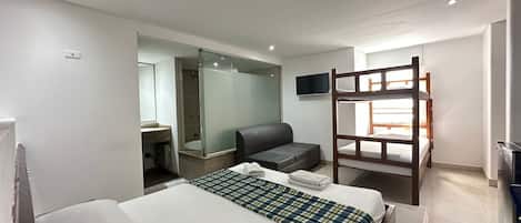 A hotel room with a bed, a sofa, a TV, a bunk bed, and a shower area.
