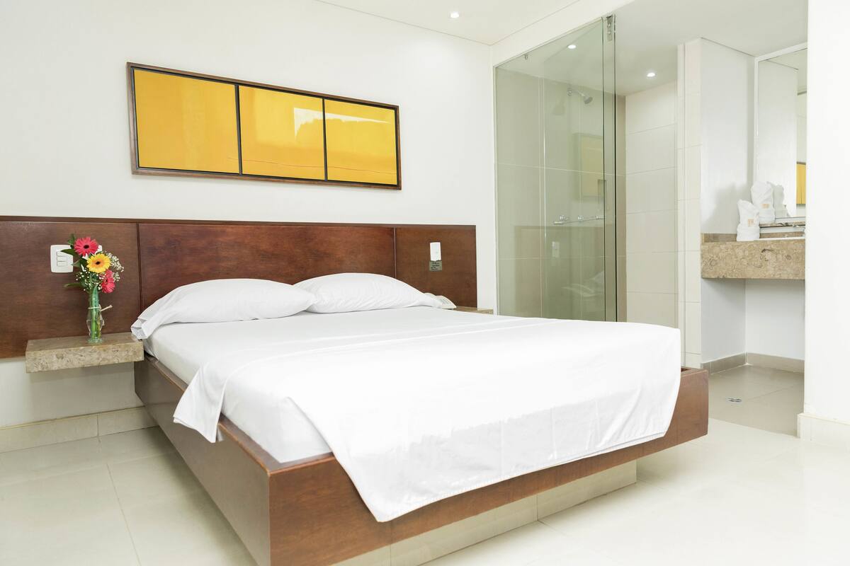 Habitación de hotel moderna con una cama grande, cabina de ducha de vidrio y tocador con encimera de mármol.