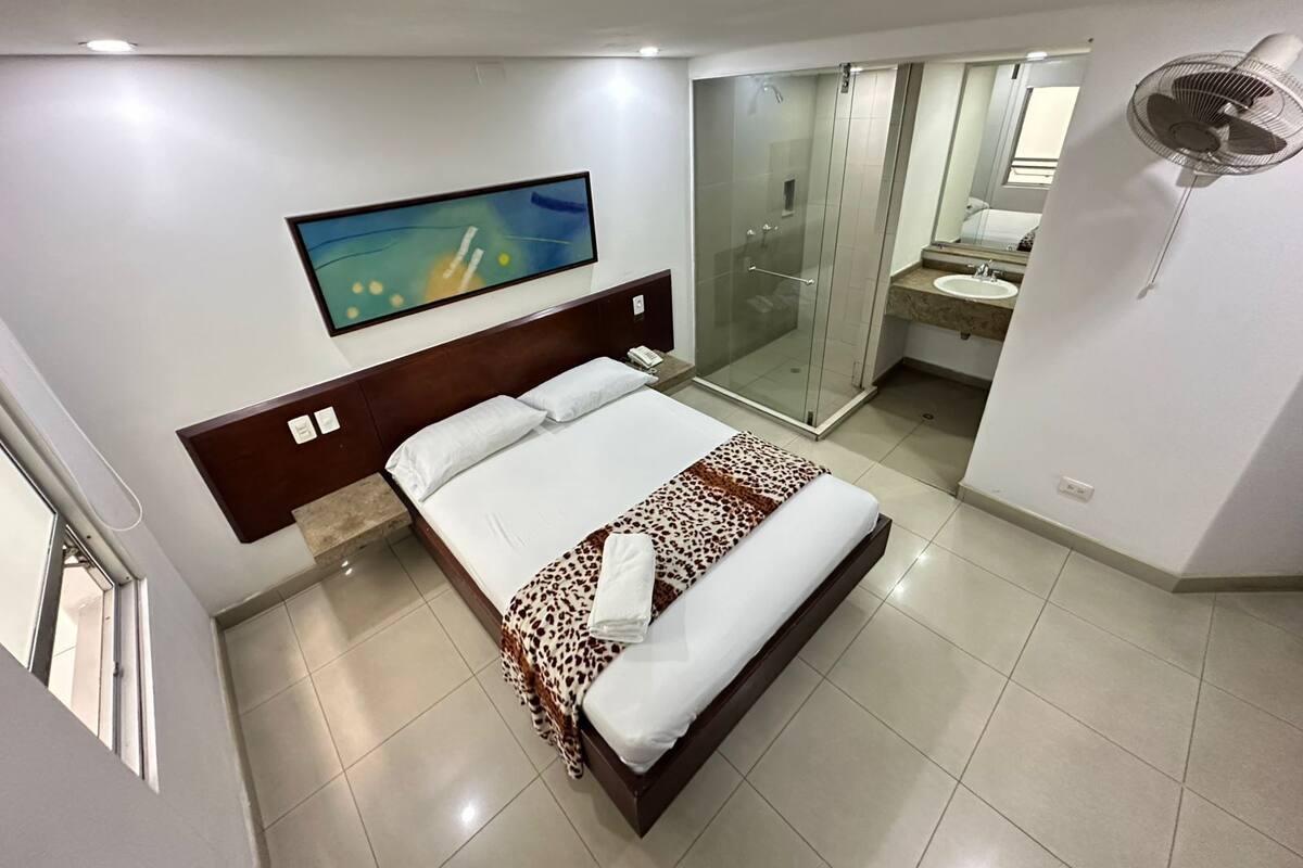Una habitación de hotel con cama, ducha, baño y un cuadro en la pared.