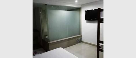 A hotel room with a bed, a television mounted on the wall, and a sliding door leading to a bathroom.