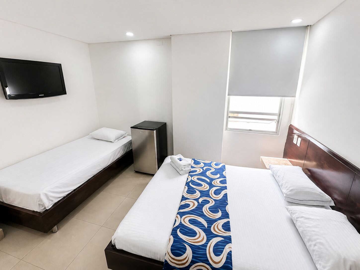 Une chambre d’hôtel avec deux lits simples, un téléviseur fixé au mur, un petit réfrigérateur et une fenêtre donnant sur un paysage agréable.