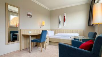 Ein Hotelzimmer mit einem Bett, einem Schreibtisch, zwei Stühlen, einem kleinen Tisch, einer Lampe und Kunstwerken an den Wänden.