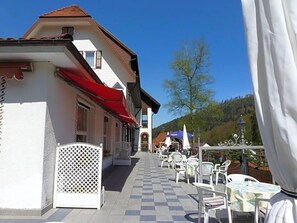 An outdoor seating area with tables and chairs, a building with a red awning, and a clear blue sky.