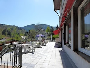 An outdoor patio with tables and chairs, a railing, and a view of a mountain.