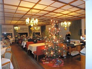 A dining area with tables and chairs, a Christmas tree, and chandeliers.