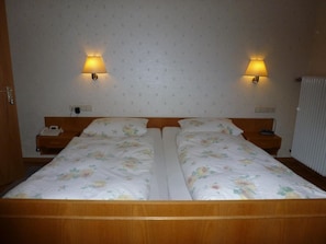 A double bed with floral bedding, two bedside lamps, a bedside telephone, and a radiator.