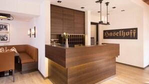 Una recepción con detalles de madera, una zona de estar con un sofá marrón, y un letrero en la pared con el nombre 'Haselhof'.