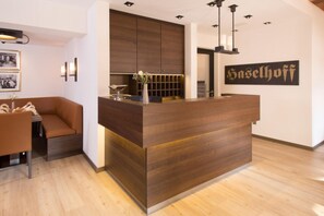Un comptoir d’accueil avec un revêtement en bois, un espace détente avec un canapé marron et une enseigne fixée au mur portant le nom « Haselhof ».