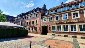 Un hotel con fachada de ladrillo tradicional, entrada central y un patio con pavimento estampado.