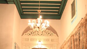 Een slaapkamer met een hemelbed, een versierd plafond en een kroonluchter.