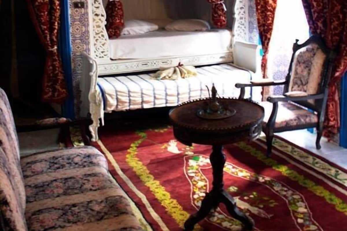 Ein Zimmer mit einem Bett, einem Sessel, einem kleinen Tisch und einer dekorativen Decke.