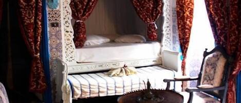 Una habitación con cama, una silla, una mesita y un techo decorativo.