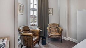 Ein Zimmer mit zwei Ledersesseln, einem Heizkörper, einem Fenster mit Blick und einem gerahmten Bild an der Wand.