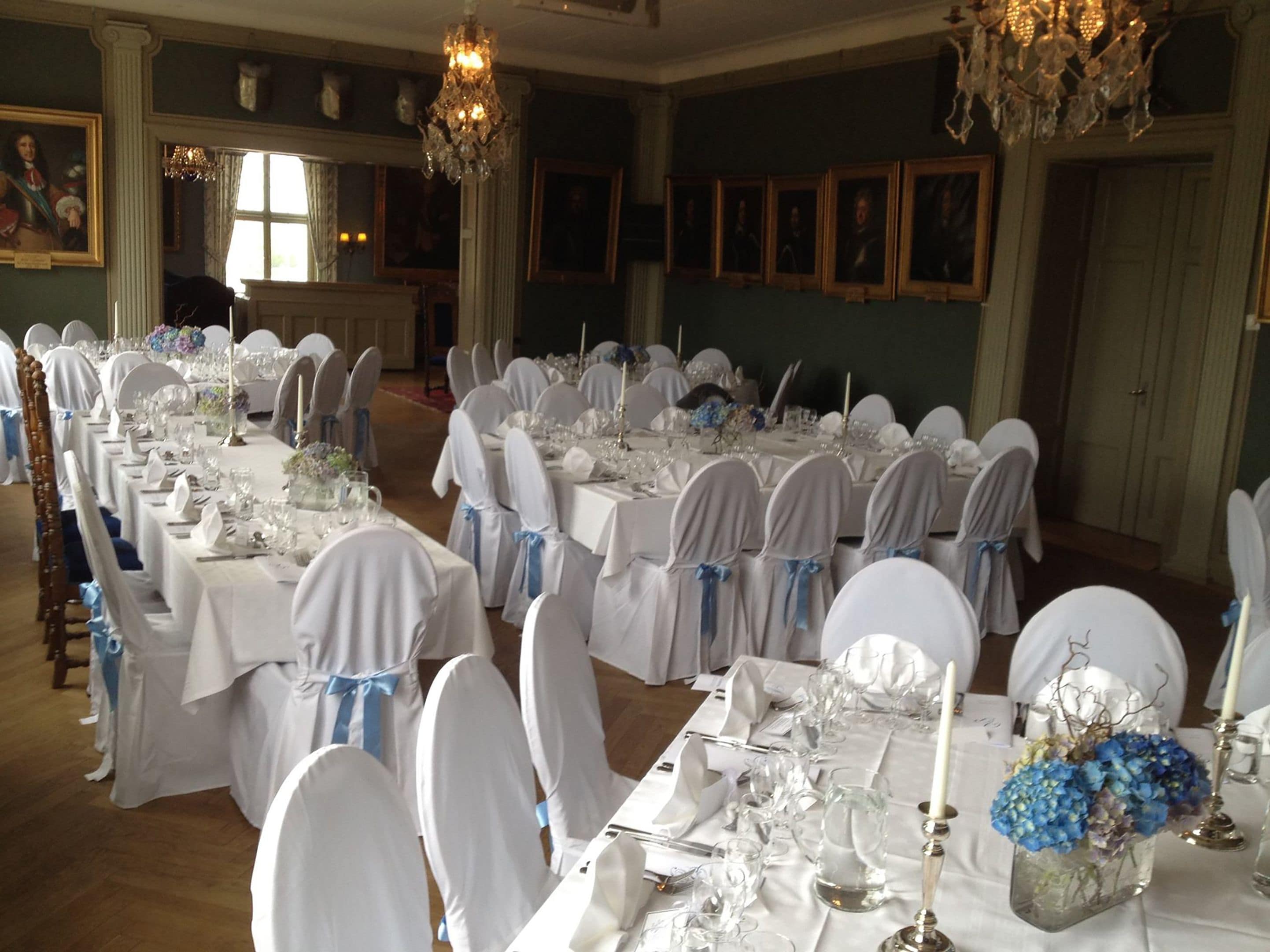 A banquet hall with long tables set for a formal event, adorned with white tablecloths and blue sashes.