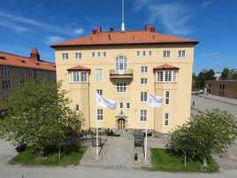 En stor, gul byggnad med ett rött tegeltak, många fönster och två flaggor.