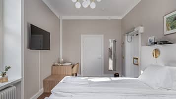 A hotel room with a bed, a desk, a chair, a television, and a shower area.