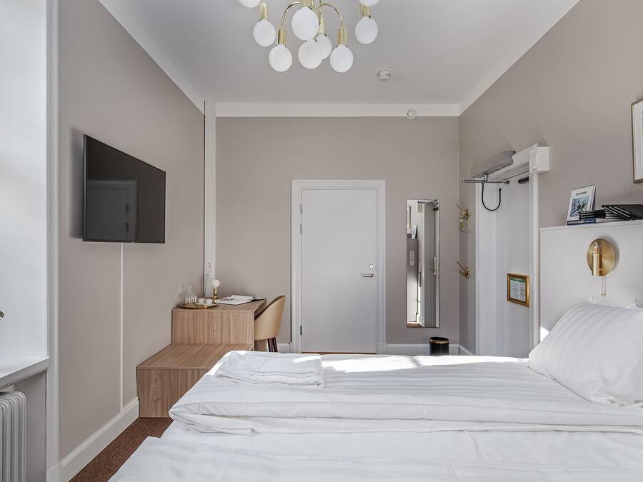 A hotel room with a bed, a desk, a chair, a television, and a shower area.