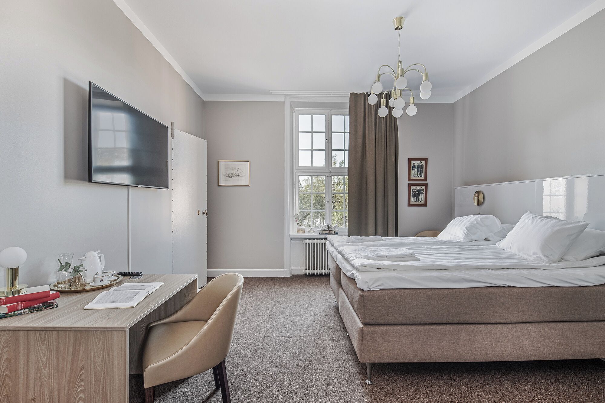 Una camera d'albergo con un letto, una scrivania con una sedia, un televisore e una finestra con tende.