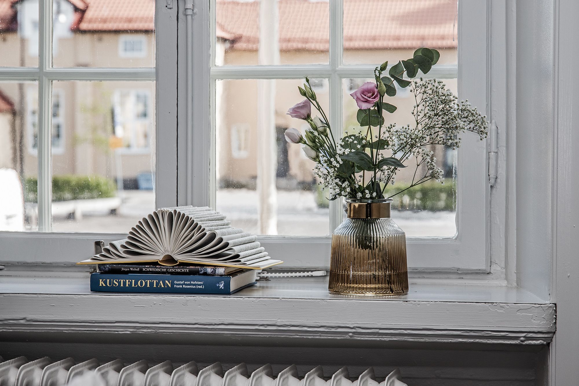 Un rebord de fenêtre orné d’un livre intitulé « Kustflotten » et d’un vase rempli de fleurs.